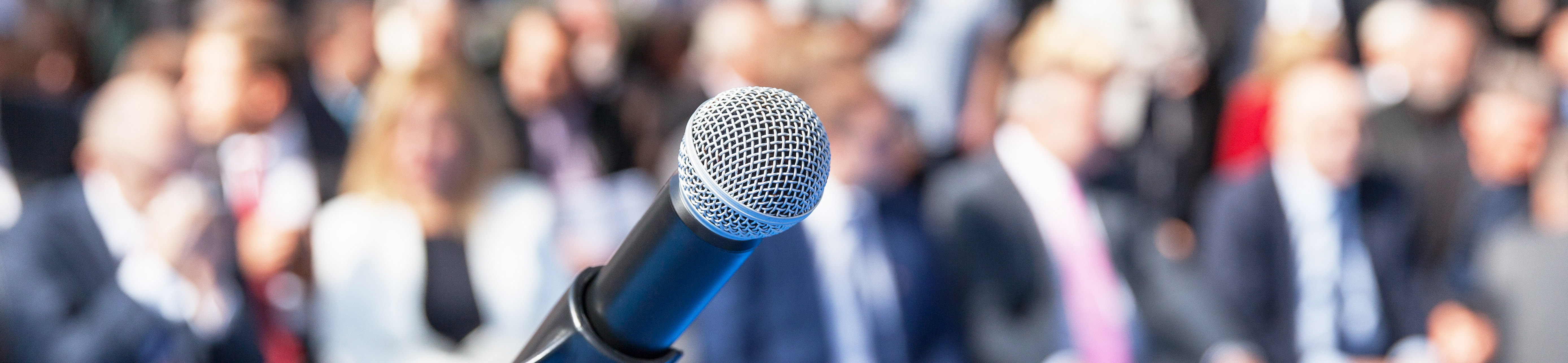 Image of a microphone with audience in the background